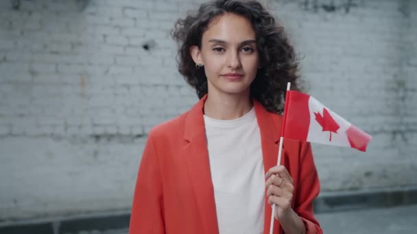 Retrato em câmera lenta de mulher de cabelos encaracolados em pé ao ar livre com a bandeira canadense sorrindo — Vídeo de Stock