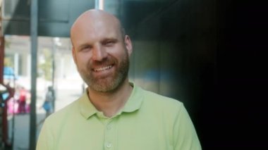 Kendine güveni olan bir gencin şehir arka planında gülümseyerek durduğu yavaş çekim portresi.