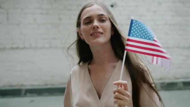 Portrait de jolie jeune femme debout à l'extérieur avec drapeau américain souriant regardant la caméra — Video