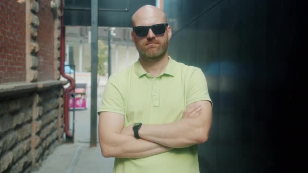 Langsom bevægelse portræt af stilfuld ung mand stående med arme krydsede udendørs iført moderne solbriller – Stock-video