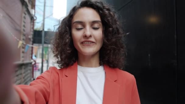 POV portrait de femme gaie avec des cheveux bouclés bavarder et agiter la main faire appel vidéo à l'extérieur en ville — Video