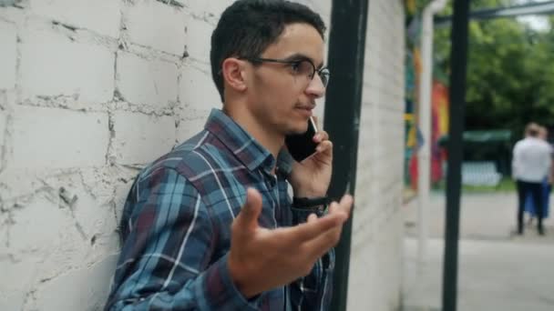 Joyful Arab man chatting on mobile phone and smiling standing outdoors in city on summer day — Stock Video