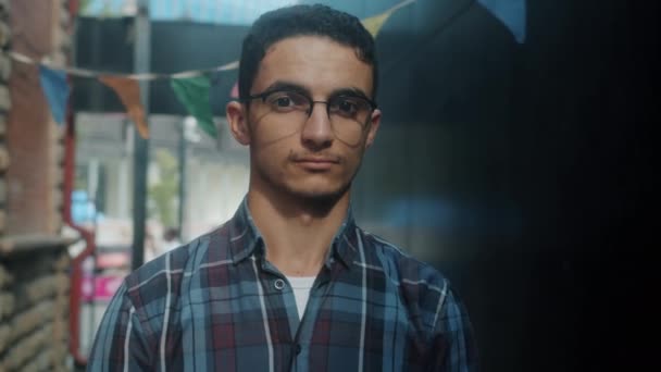 Retrato en cámara lenta del atractivo hombre de Oriente Medio con gafas mirando a la cámara con una sonrisa ligera — Vídeo de stock