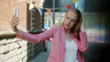 Şehrin arka planında akıllı telefon kamerasıyla selfie çeken güzel bir genç kadının portresi.