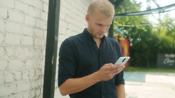 Movimiento lento del joven alegre usando el teléfono inteligente afuera sonriendo de pie solo tocando la pantalla — Vídeo de stock