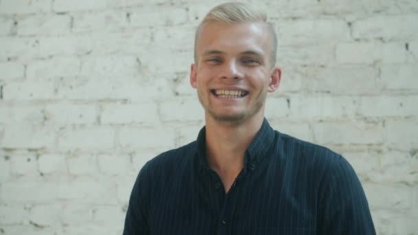 Fröhlicher junger Mann lächelt und lacht im Freien mit Backsteinmauer im Hintergrund — Stockvideo