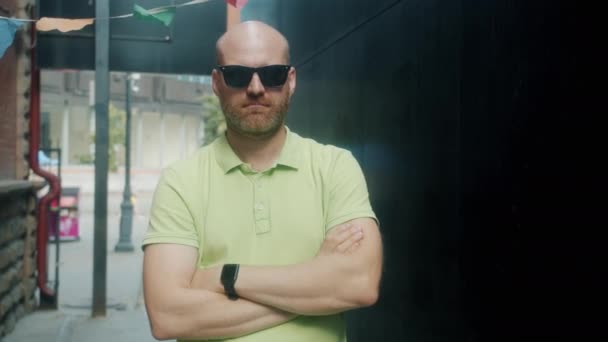 Portret van een serieuze jongeman die een zonnebril afdoet en naar de camera kijkt tegen een stedelijke achtergrond — Stockvideo