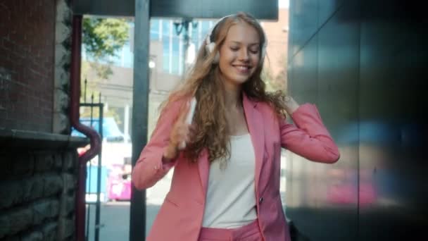 Retrato de una joven feliz disfrutando de la música a través de auriculares caminando sosteniendo el teléfono inteligente en la calle de la ciudad — Vídeos de Stock