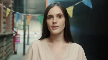 Çekici öğrenci portresi. Kahverengi saçlı ve çilli güzel bir kız. Sokakta tek başına gülümsüyor.