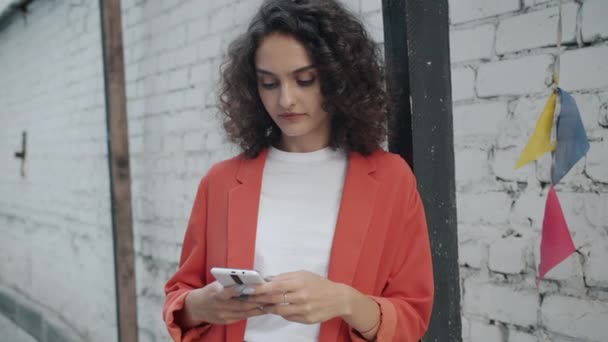 Şehir sokaklarında akıllı telefon ekranına bakarak gülümseyen mutlu bir kızın ağır çekimde portresi. — Stok video