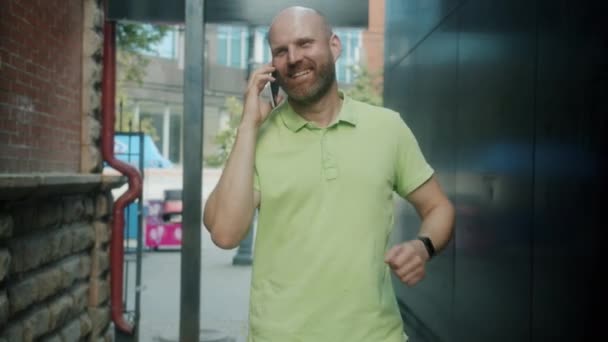 Hombre joven con ropa casual caminando al aire libre charlando en el teléfono móvil en el día de verano — Vídeo de stock