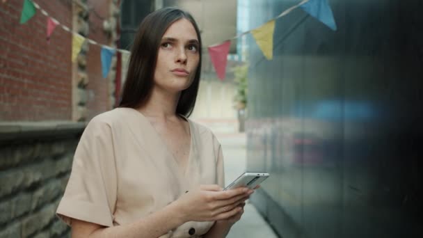 Retrato en cámara lenta de mujer atractiva usando la pantalla táctil del teléfono inteligente y mirando alrededor al aire libre — Vídeo de stock