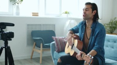 Mutlu genç melez adam gitar sallıyor ve çevrimiçi blog için konuşma videosu çekiyor.