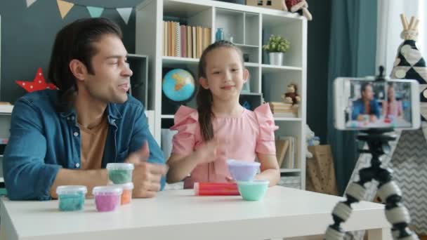 Kind vlogger opname video over spelen deeg zitten aan tafel met vader en met behulp van smartphone camera — Stockvideo