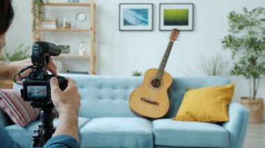 Yakışıklı vlogger video kamera ayarlıyor sonra gitar çalıyor ve el sallıyor.