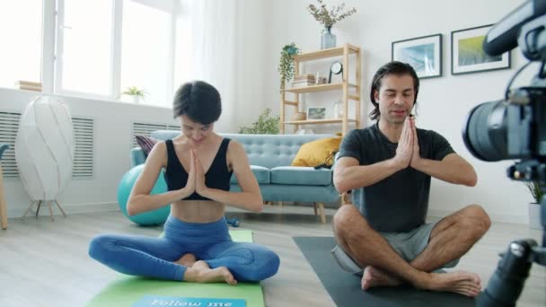 Uomo e donna vlogger meditando poi mostrando seguimi segno e facendo il cinque seduti su stuoie yoga — Video Stock