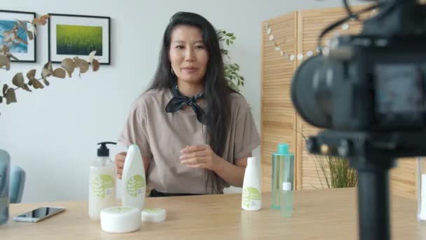 Moderno blogger asiático hablando de cosméticos ecológicos mostrando un gesto de pulgar hacia arriba y saludando con la mano mirando a la cámara — Vídeos de Stock