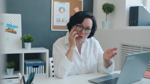 Kobieta przedsiębiorca omawia biznes na telefon komórkowy i korzystania z laptopa w nowoczesnym biurze — Wideo stockowe