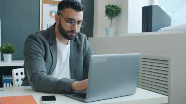Несчастный бизнесмен, работающий с ноутбуком, ударяющий кулаками по столу и покидающий офис — стоковое видео