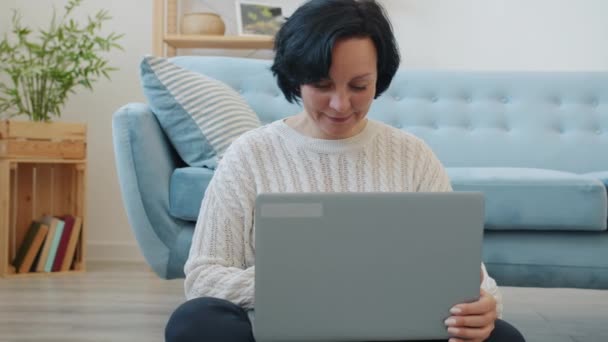 Mujer sonriente utilizando la escritura portátil y luego apagar el ordenador y pensar en interiores en casa — Vídeo de stock