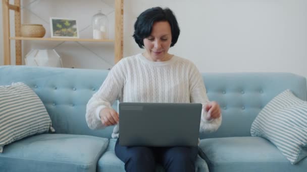 Повільний рух збудженої леді, використовуючи ноутбук, що піднімає руки, насолоджуючись хорошими новинами в квартирі — стокове відео
