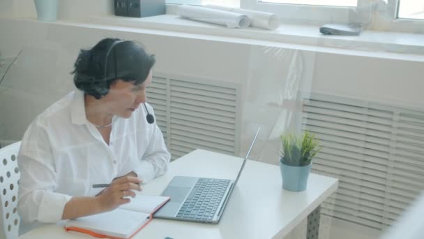 Kulaklık takan ciddi bir kadın bilgisayar ekranına bakıyor ve ofiste yazıyor. — Stok video