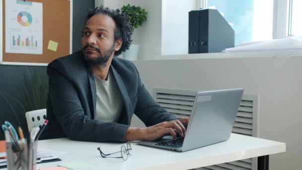 Pensivo homem do Oriente Médio trabalhando com laptop e pensando sentado na mesa no escritório — Vídeo de Stock