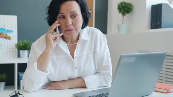 Zelfverzekerde volwassen vrouw opnemen van audioberichten en glimlachen genieten van online communicatie op kantoor — Stockvideo