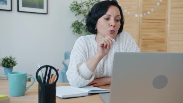 Allvarlig kvinna chattar på videosamtal med bärbar dator hemma och skriver på nätet under en pandemi — Stockvideo