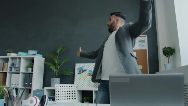 Привлекательный работник танцует под музыку, развлекаясь в помещении на работе. — стоковое видео