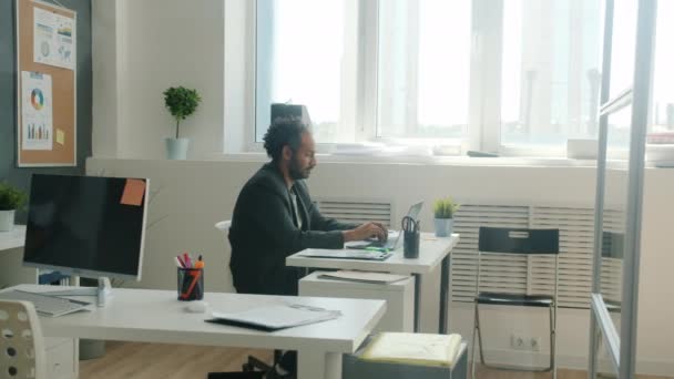 Zijaanzicht van ernstige mannelijke kantoormedewerker met behulp van laptop alleen in creatieve ruimte — Stockvideo