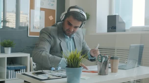 Trabalhador de escritório alegre homem se divertindo usando fones de ouvido tocando bateria imaginária na mesa — Vídeo de Stock