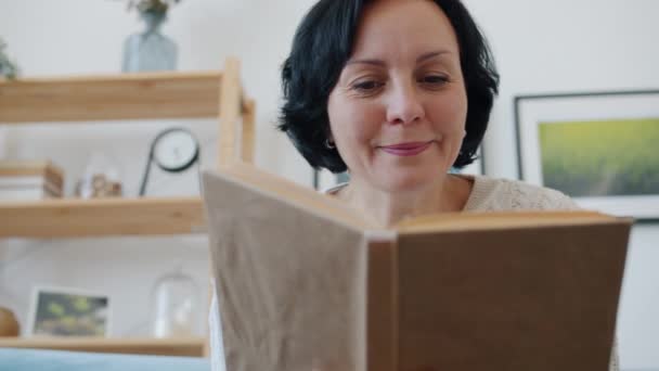 Powolny ruch wesołej pani czytanie książki i uśmiech wewnątrz mieszkania — Wideo stockowe