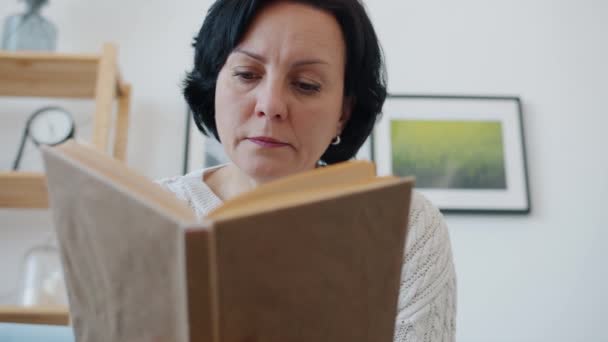 Serious maduro señora leyendo libro disfrutando de la literatura sentado en el interior de casa — Vídeos de Stock