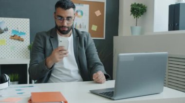 Neşeli iş adamı akıllı telefon ekranına bakıyor ve işteki başarıyı kutluyor