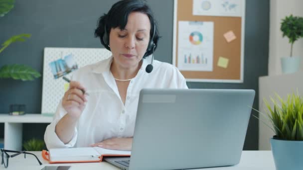 Trage beweging van het bedrijfsleven dame het dragen van een hoofdtelefoon met microfoon schrijven en kijken naar laptop scherm — Stockvideo