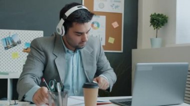 Kulaklık takan neşeli iş adamı ofiste müzik dinlemekten zevk alıyor.