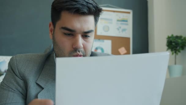 Jovem empresário pensativo olhando para papéis e pensando sobre o desenvolvimento de negócios no escritório — Vídeo de Stock