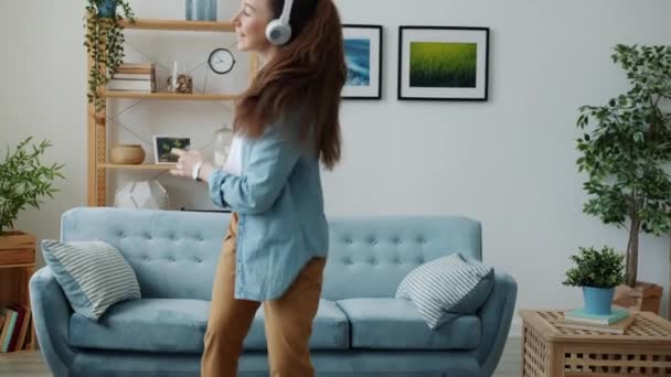 Jeune femme mignonne portant des écouteurs dansant et chantant à distance à la maison — Video