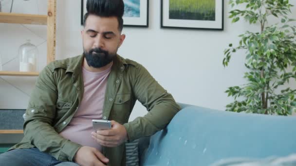 Orta Doğulu bir adam akıllı telefon kullanıyor. Kötü haberler alıyor. Evdeki kanepede oturmuş kafasını sallıyor. — Stok video