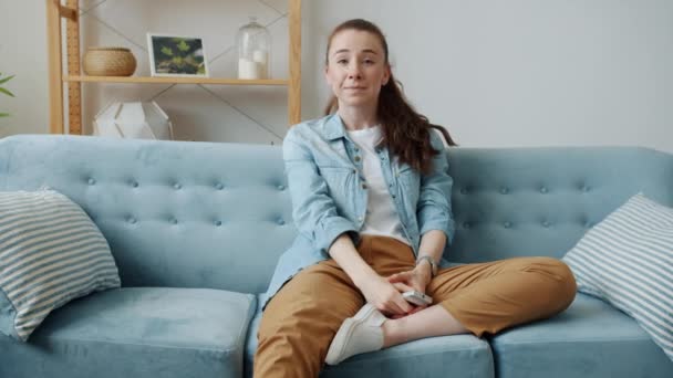 Porträtt av söt kvinnlig student tittar på rolig komedi på TV och skrattar sitter på soffan hemma — Stockvideo