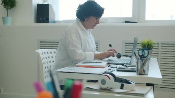 Trage beweging van ambitieuze zakenvrouw werken met laptop en schrijven in notebook op kantoor — Stockvideo