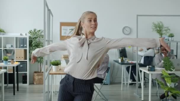 Emocionada joven empresaria que se muda a la música en la oficina mientras la gente de fondo aplaude — Vídeo de stock