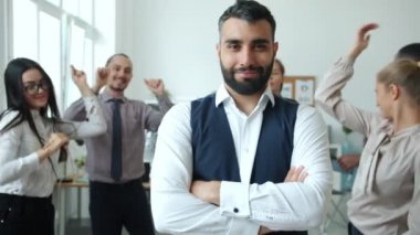 Çalışan hırslı bir ofis çalışanı, neşeli iş arkadaşları müzikle dans ederken gülümsüyor.
