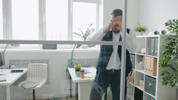 Радостный бизнесмен танцует в стеклянном офисе, наслаждаясь отдыхом в одиночестве — стоковое видео