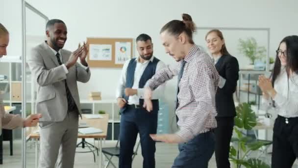 Wolny ruch twórczego faceta tańczącego w biurze w gronie klaskających współpracowników — Wideo stockowe