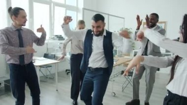 Meslektaşlar eğlenirken ve alkışlarken resmi giyimli bir adamın ofiste dans etmesi.