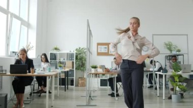 İş arkadaşları arka planda el çırparken güzel sarışın ofiste dans ediyor.