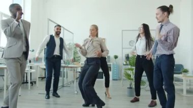 Yavaş hareket eden neşeli çalışanlar dans ederek iş başarısını kutluyor.