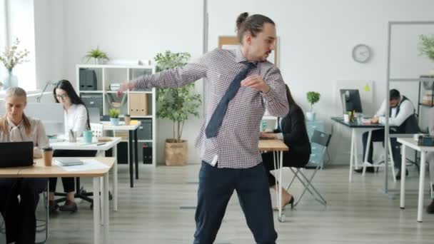 Kreatywny młody człowiek tańczący w biurze patrząc przed kamerą, kiedy dołącza do niego grupa współpracowników — Wideo stockowe